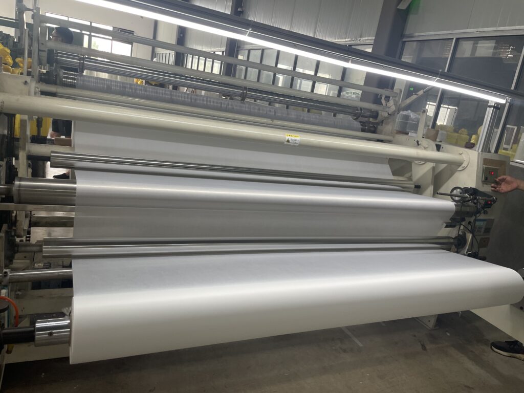 A large industrial roll of white non-woven fabric ready for processing