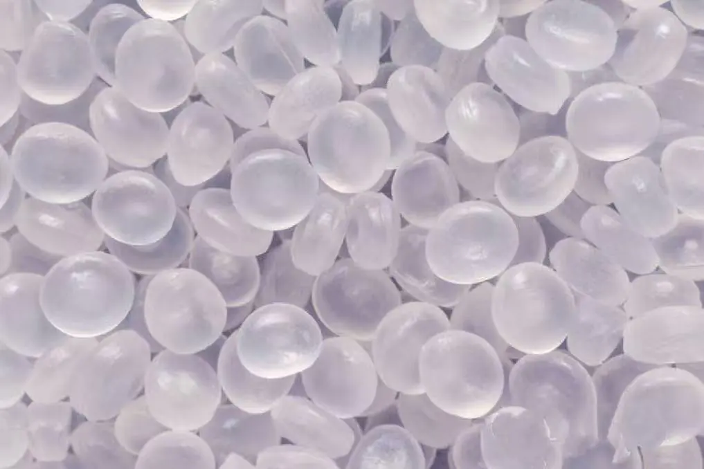 A close-up of shiny plastic pellets, the raw material for polyester and polypropylene fibers